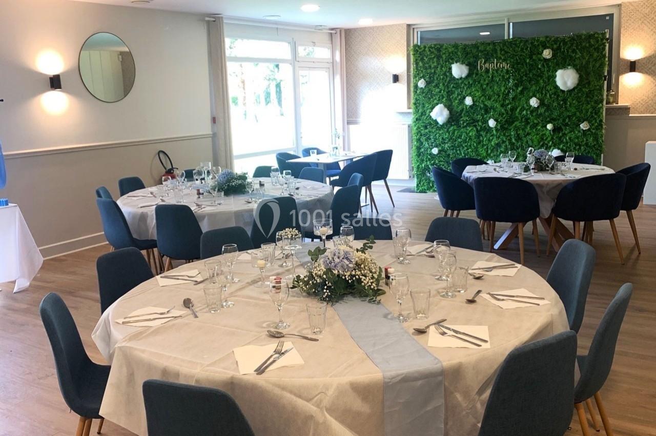 Salle de réception décorée avec des tables rondes dressées, des chaises bleues et un mur végétal en arrière-plan.