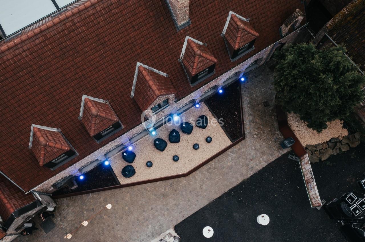 Vue aérienne d'une cour pavée avec des toits en tuiles, des tables rondes et des lumières bleues installées.