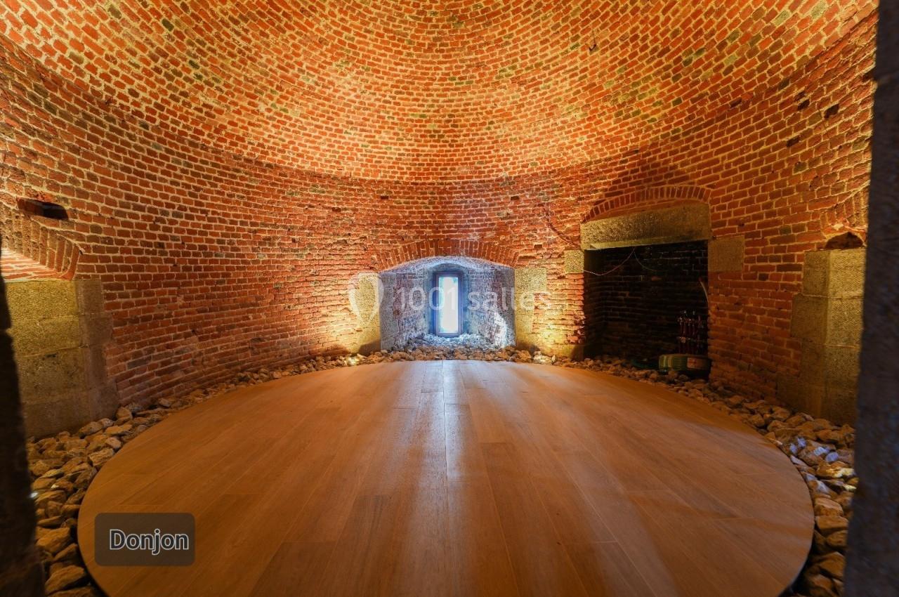 Salle circulaire en briques rouges avec un sol en bois, éclairée par une lumière naturelle provenant d'une ouverture…