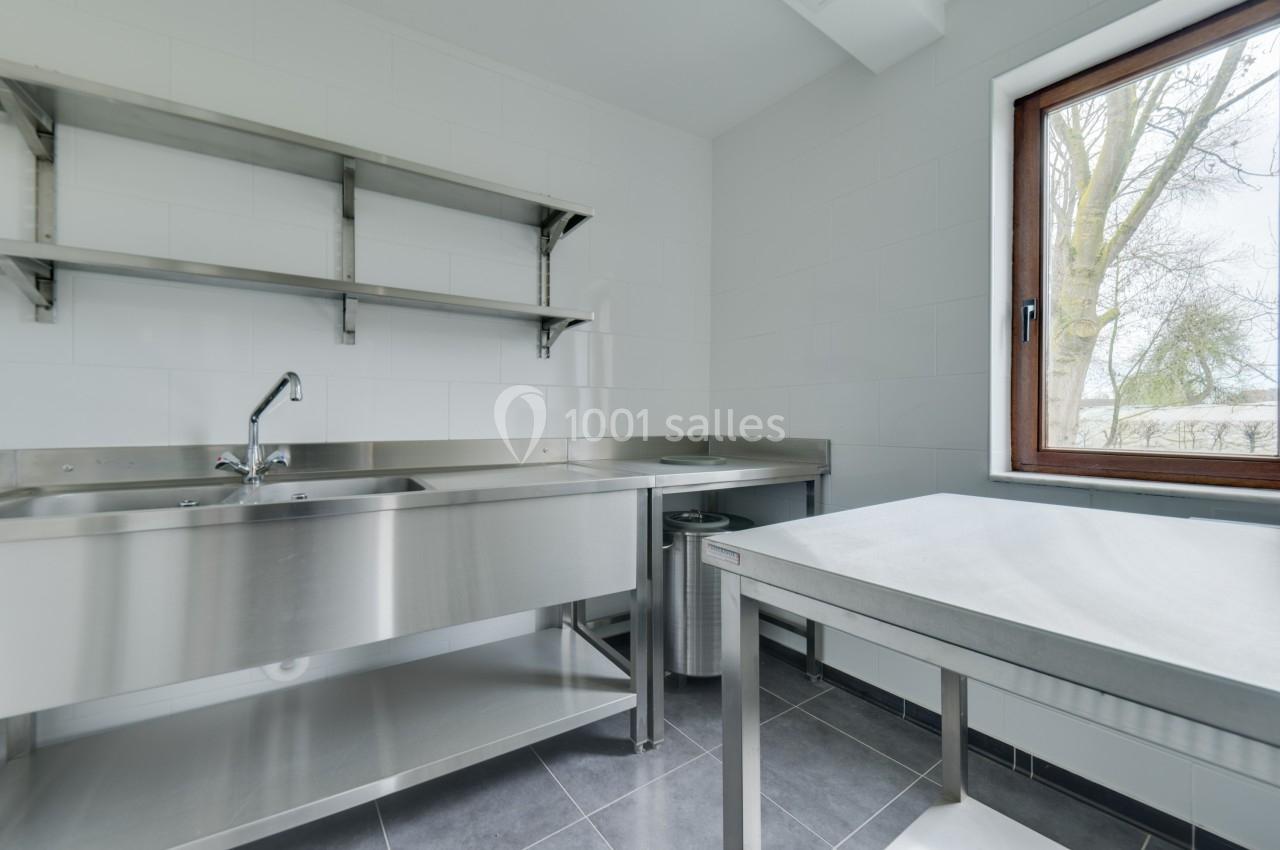 Cuisine professionnelle avec évier en inox, étagères murales, plan de travail et fenêtre donnant sur l'extérieur.