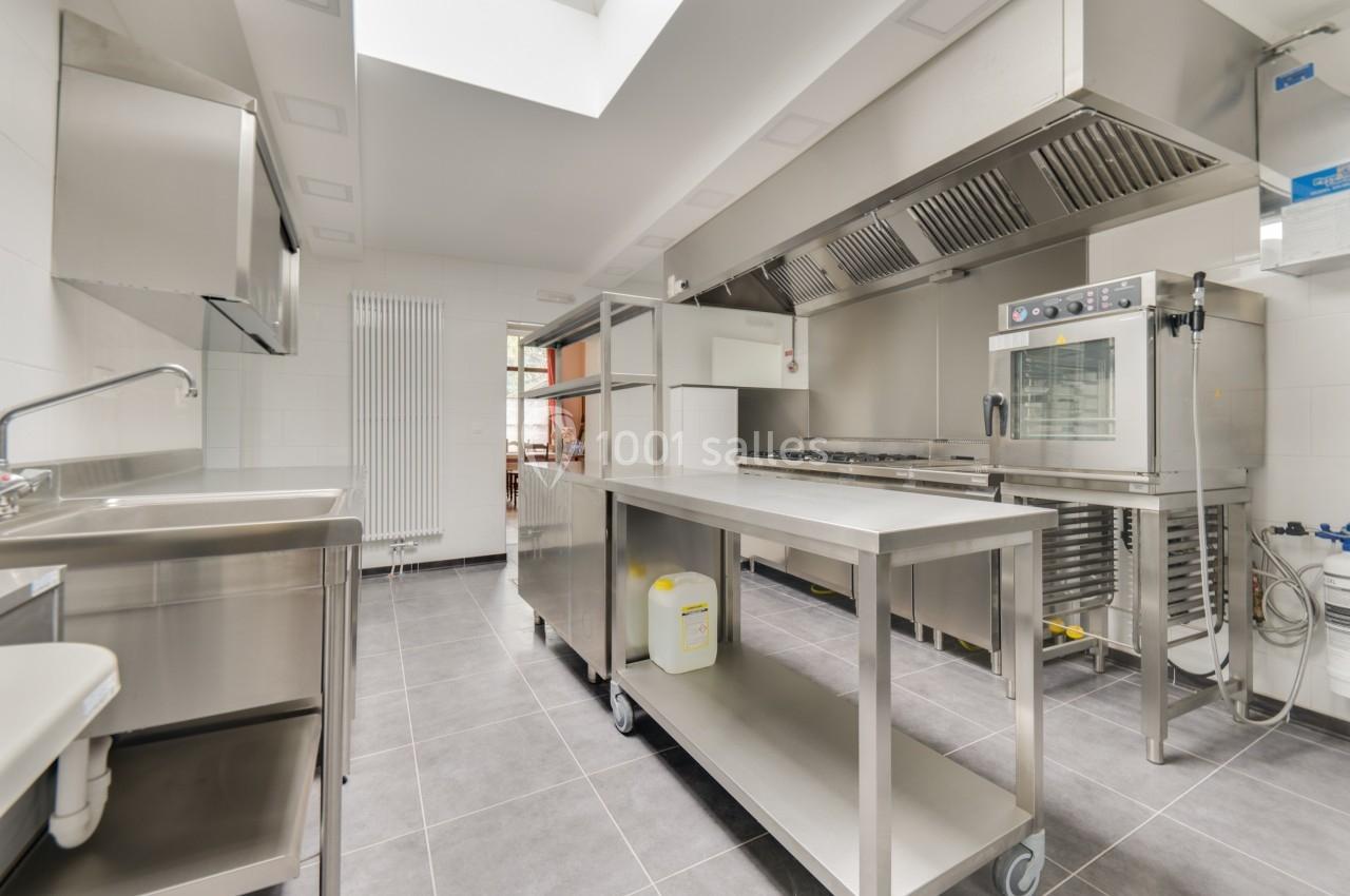 Cuisine professionnelle moderne avec équipements en inox, plan de travail, évier, four et hotte dans un espace lumineux.