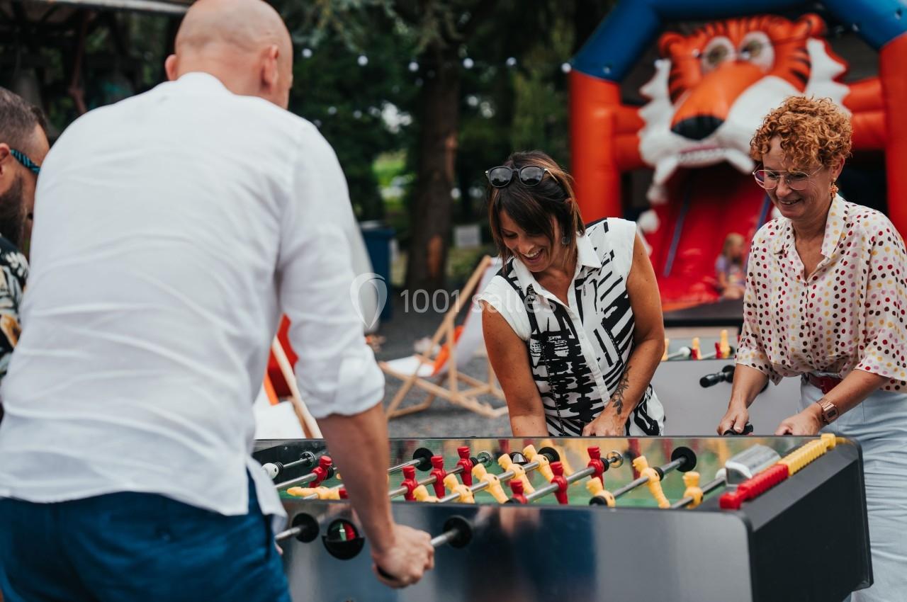 Des adultes jouent au baby-foot en extérieur, avec une structure gonflable en forme de tigre en arrière-plan.
