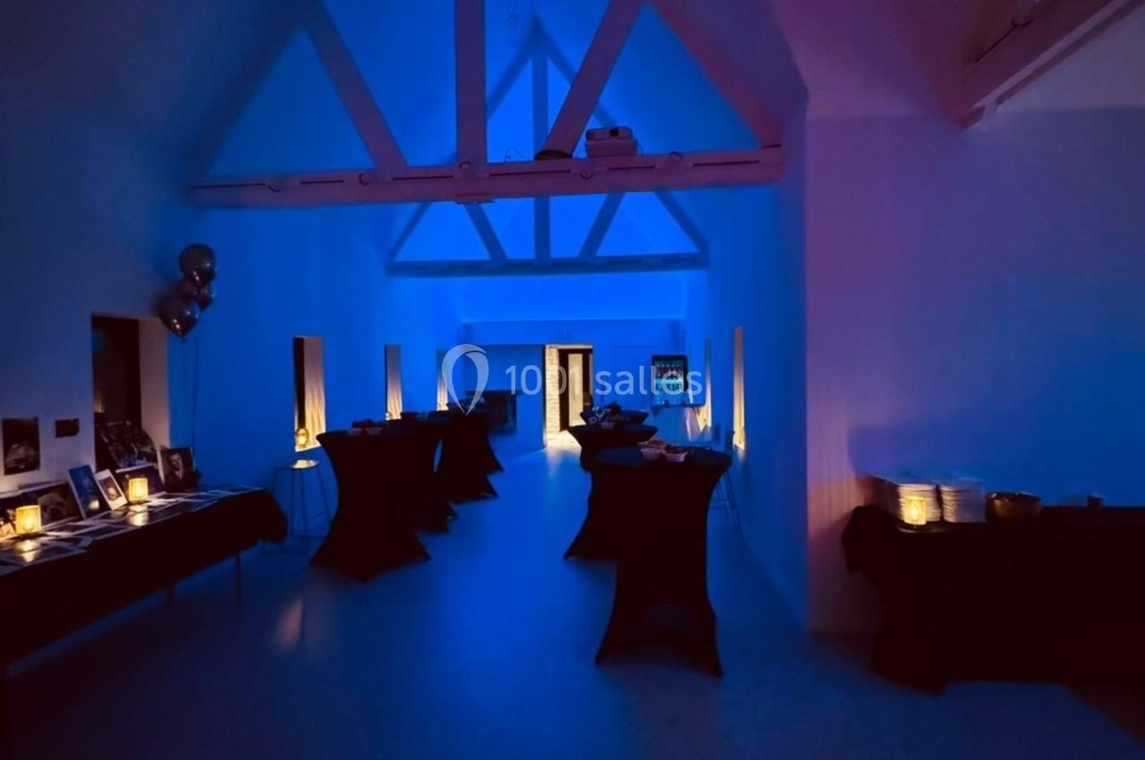 Salle éclairée par une lumière bleue tamisée, avec des tables noires dressées le long des murs.