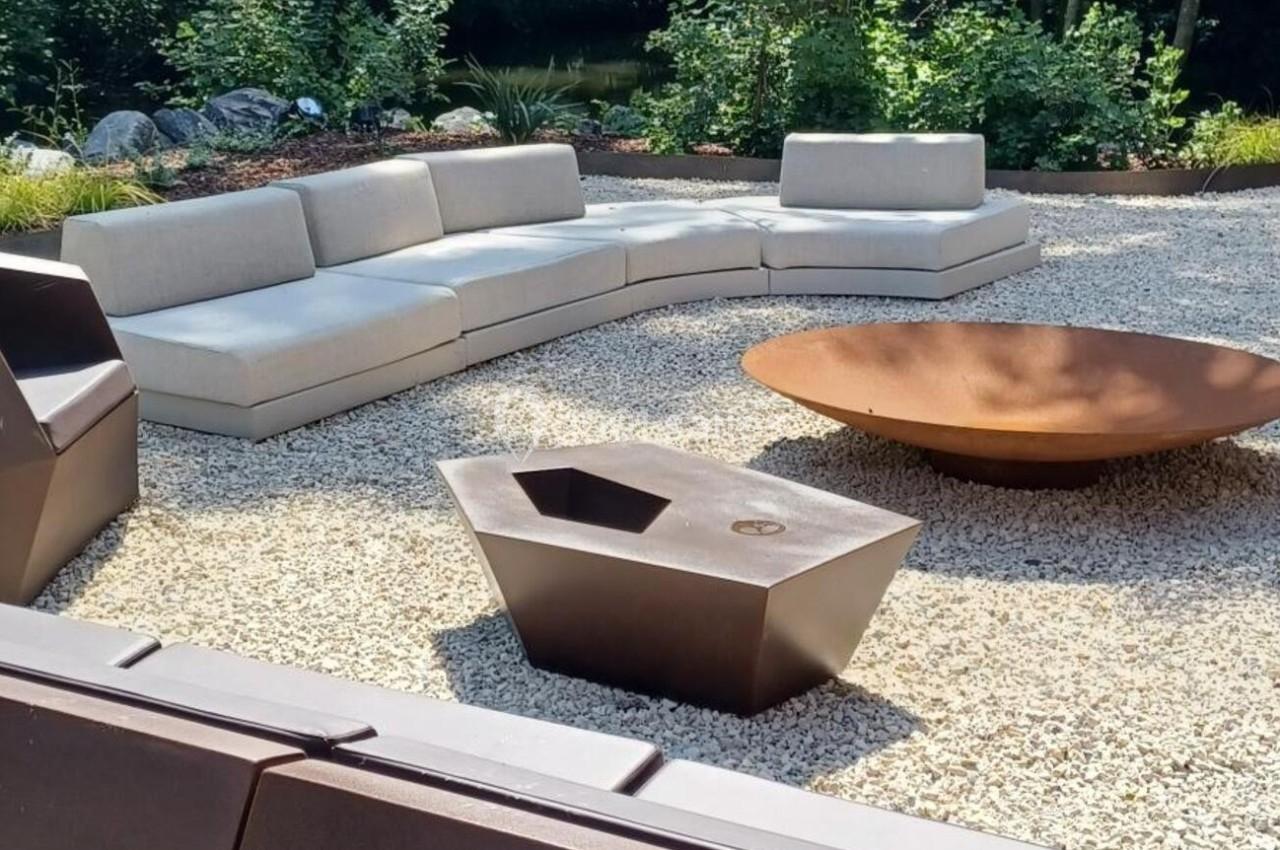 Salon de jardin moderne avec canapés et table basse sur une terrasse en gravier, entourée de végétation dense.