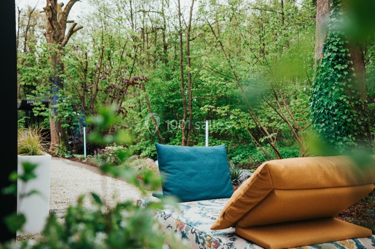 Banc extérieur avec coussins colorés, entouré de verdure et d'arbres dans un jardin paisible.