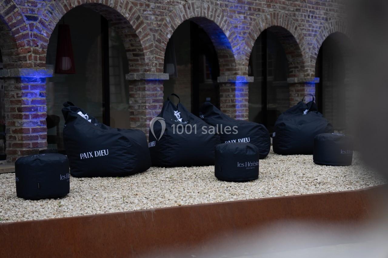 Poufs noirs marqués ’Paix Dieu’ et ’les Héritiers’ disposés sur un sol gravillonné devant un bâtiment en briques.
