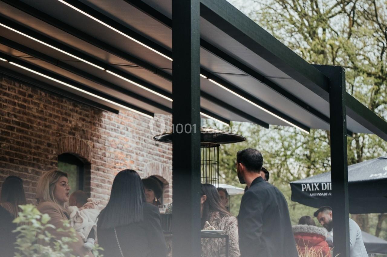 Groupe de personnes discutant sous une pergola moderne près d'un bâtiment en briques, avec des arbres en arrière-plan.