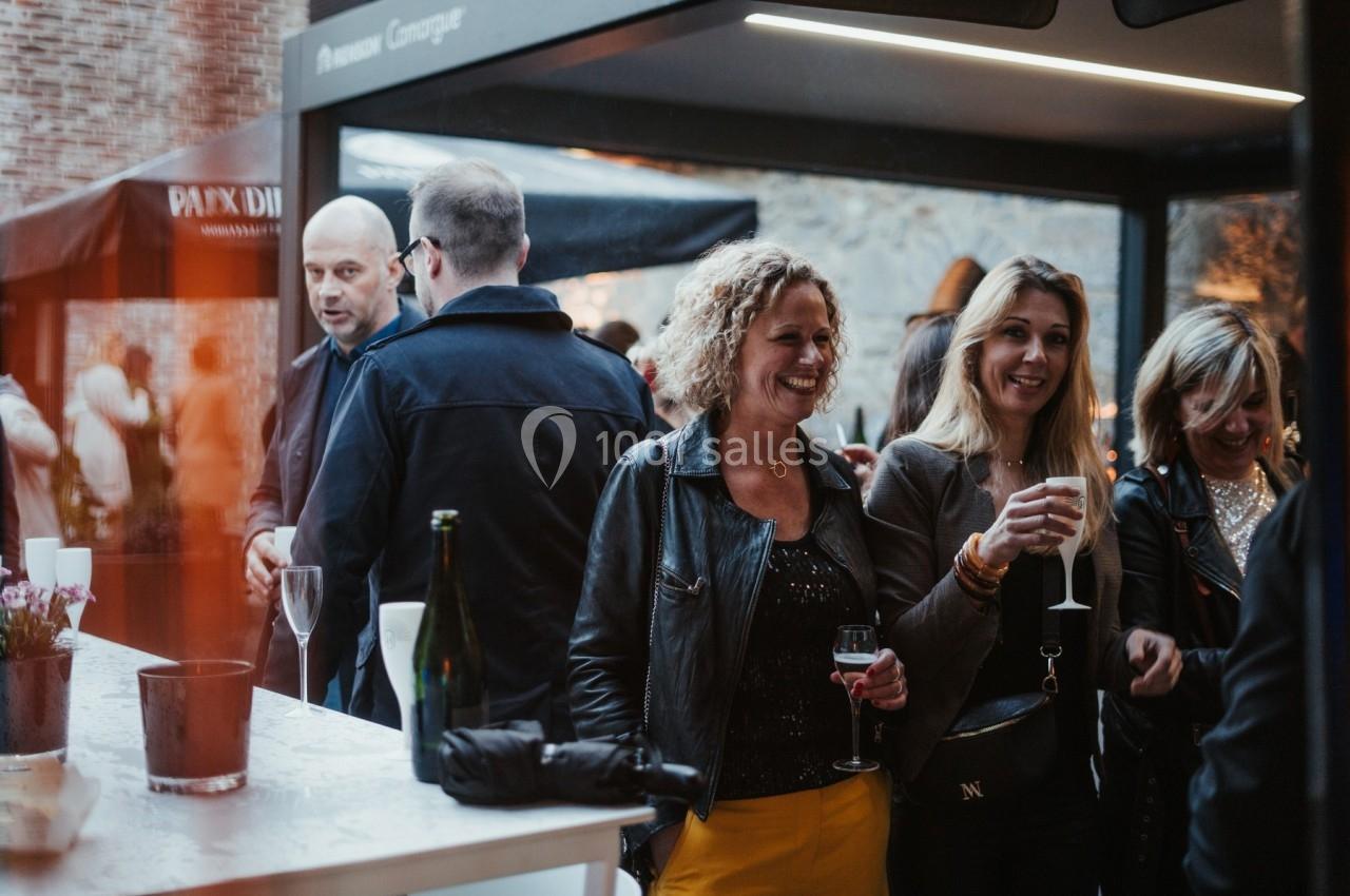 Des personnes discutent et boivent des verres lors d'un événement en extérieur, près d'un comptoir.