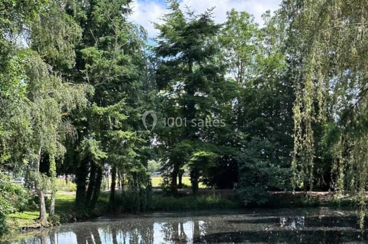 Étang entouré d'arbres avec leur reflet visible dans l'eau sous un ciel partiellement nuageux.