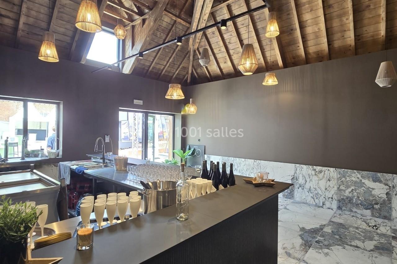 Intérieur d'un espace moderne avec un comptoir sombre, plafond en bois apparent et éclairage suspendu.