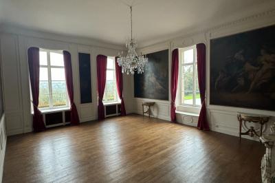 Salle élégante avec un lustre imposant, table ronde en bois, chaises vertes et grandes fenêtres encadrées de rideaux.