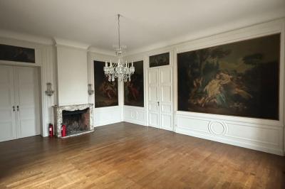 Salle élégante avec un lustre imposant, table ronde en bois, chaises vertes et grandes fenêtres encadrées de rideaux.