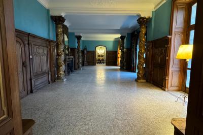 Salle élégante avec un lustre imposant, table ronde en bois, chaises vertes et grandes fenêtres encadrées de rideaux.