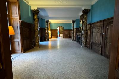 Une mariée en robe longue marche aux côtés d'un homme en costume sur une terrasse avec vue sur un paysage verdoyant.