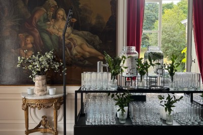 Une mariée en robe longue marche aux côtés d'un homme en costume sur une terrasse avec vue sur un paysage verdoyant.