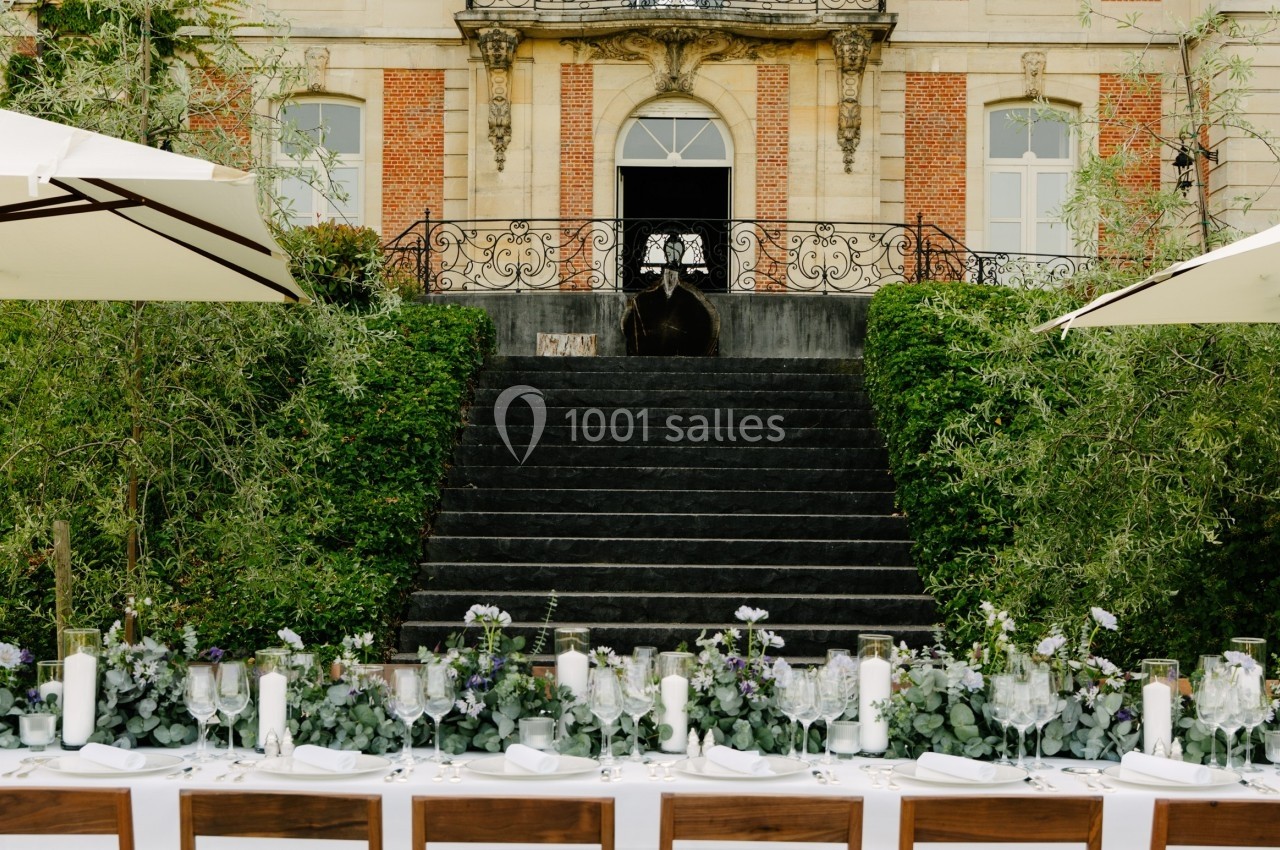 Grande table dressée avec des décorations florales devant un escalier menant à une entrée de bâtiment élégant.