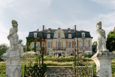 Une mariée en robe longue marche aux côtés d'un homme en costume sur une terrasse avec vue sur un paysage verdoyant.
