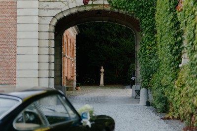 Une mariée en robe longue marche aux côtés d'un homme en costume sur une terrasse avec vue sur un paysage verdoyant.