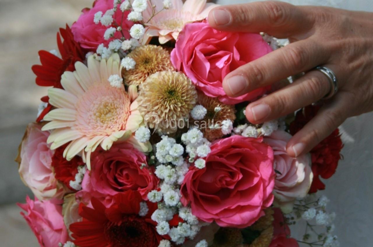 Bouquet de fleurs colorées avec des roses, des gerberas et du gypsophile, tenu par une main portant une alliance.