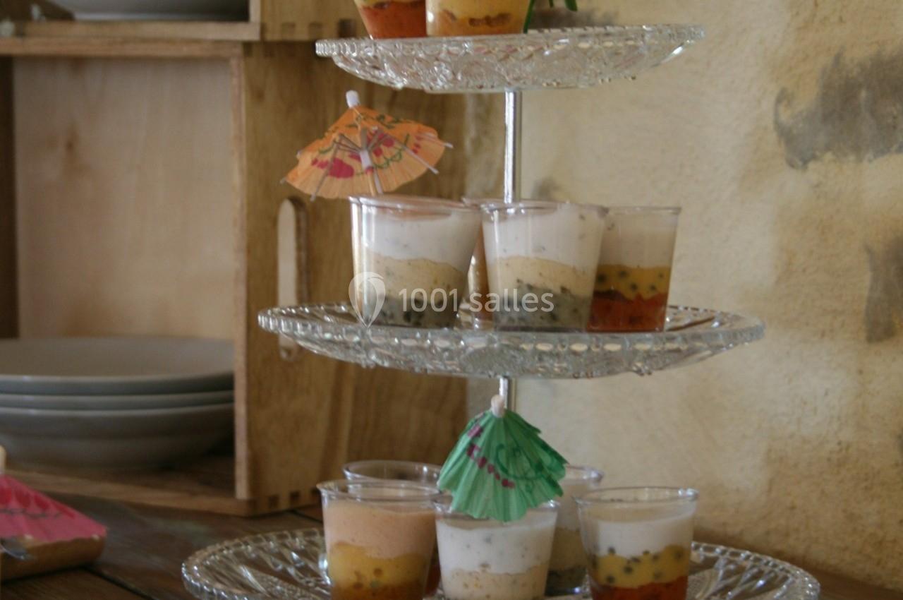 Présentoir à étages avec des verrines colorées garnies de petites ombrelles décoratives, posé sur une table en bois.