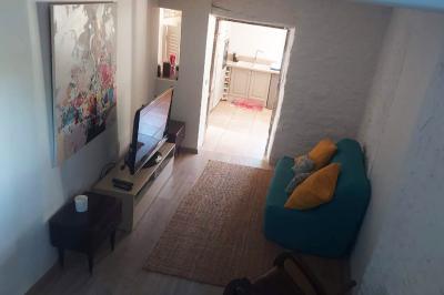 Salon lumineux avec canapé turquoise, coussins colorés, télévision, tapis en fibres naturelles et vue sur une cuisine…