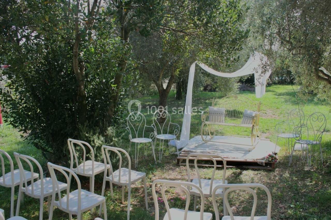 Chaises blanches disposées devant une arche décorée dans un jardin verdoyant pour une cérémonie en plein air.