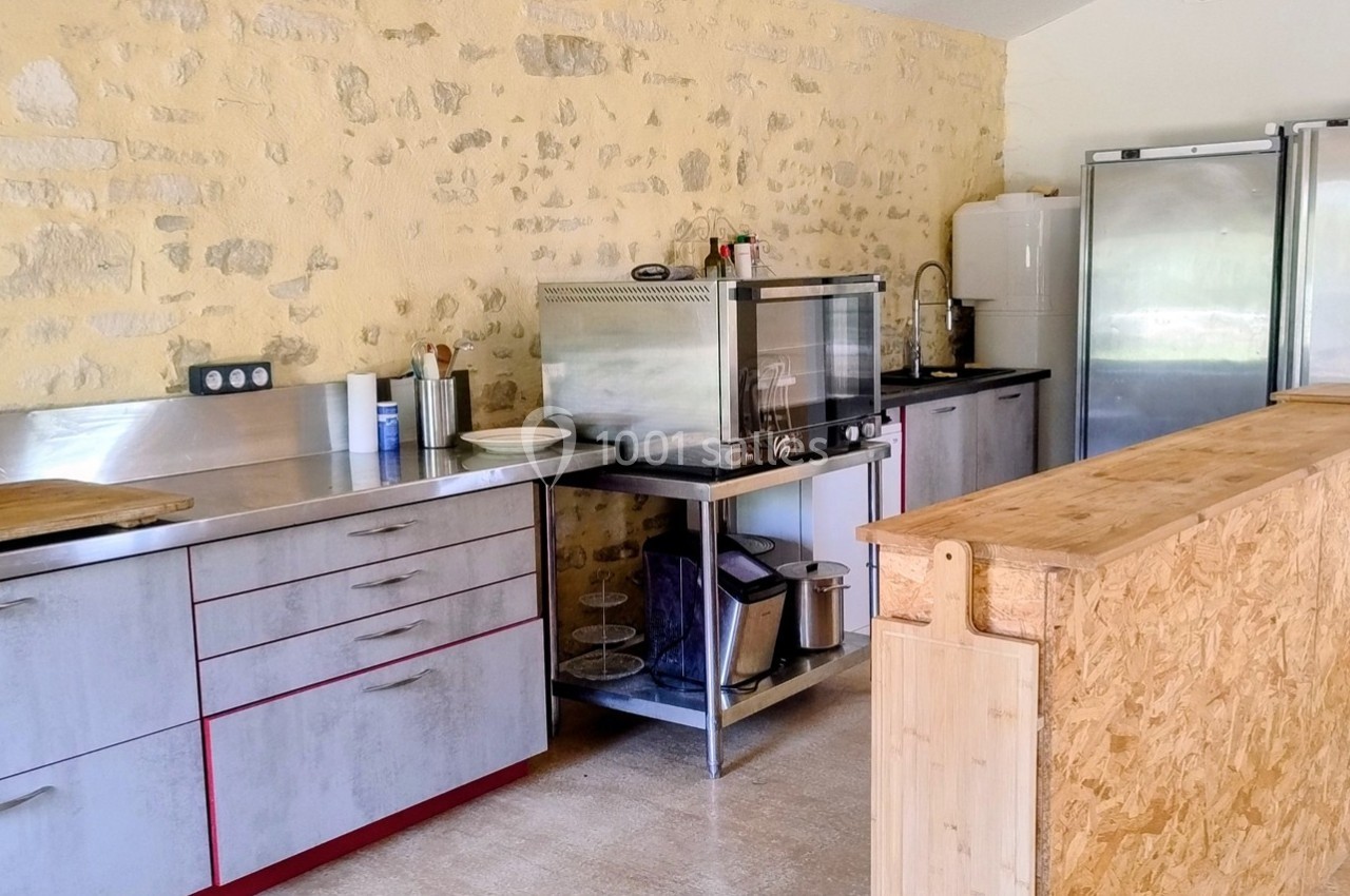 Cuisine avec un plan de travail en bois, des équipements en inox, un mur en pierre et deux réfrigérateurs argentés.