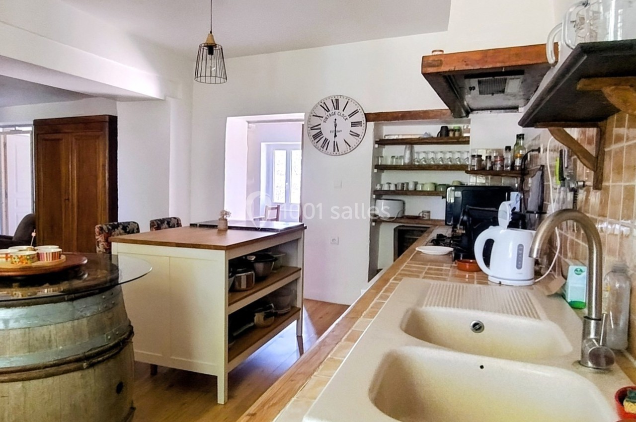 Cuisine rustique avec évier double, plan de travail en bois, étagères ouvertes et table centrale sur un tonneau.