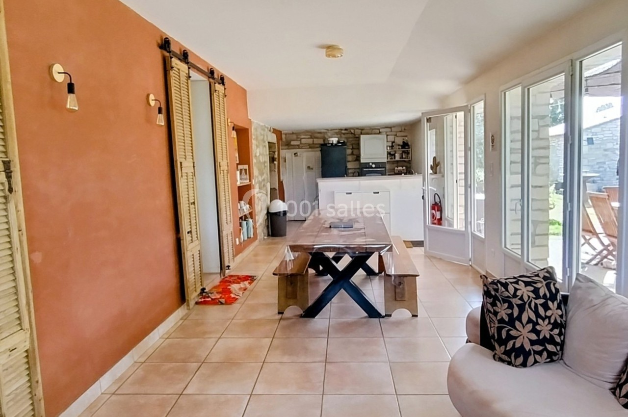 Salle à manger lumineuse avec table en bois, murs terracotta, et accès à une terrasse par des baies vitrées.