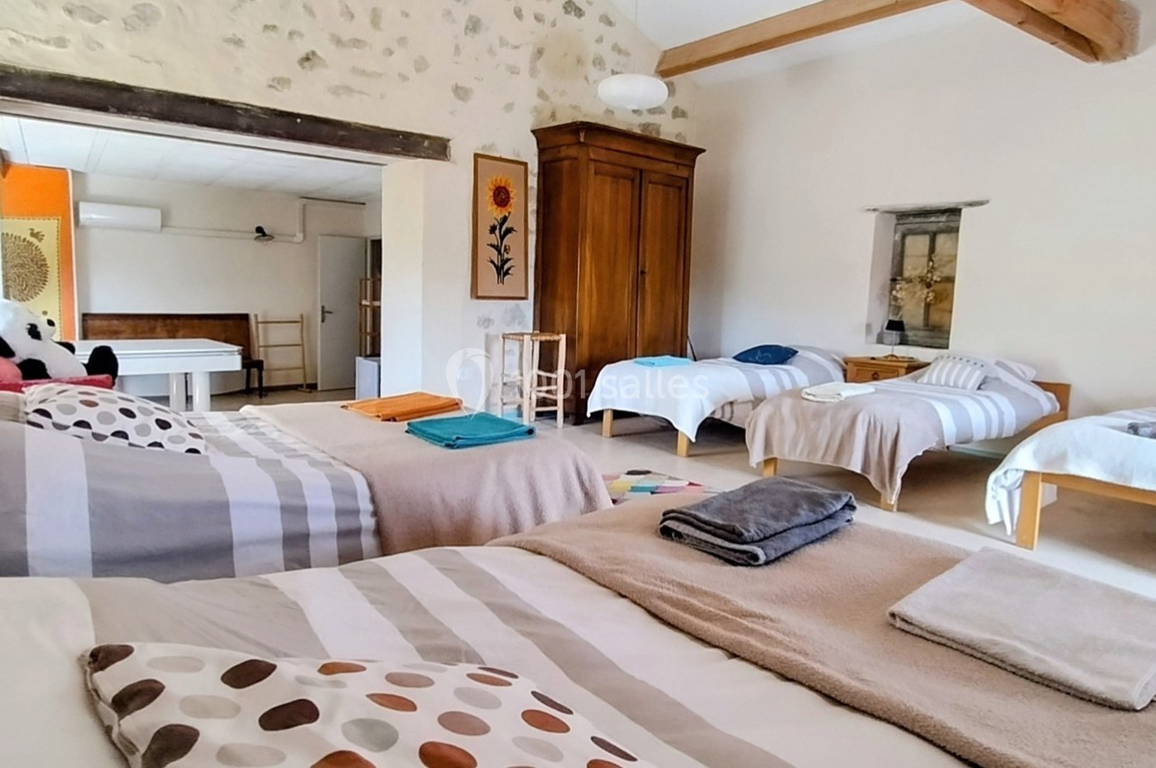 Chambre spacieuse avec plusieurs lits simples et doubles, décorée simplement avec des murs en pierre et des poutres…