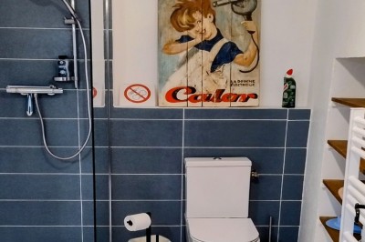 Miniature Location salle Bessas (Ardèche) - Le Mas Vie #39 Salle de bain avec douche, toilettes, étagères murales et affiche décorative au-dessus du WC.