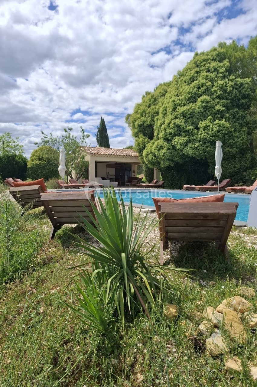 Chaises longues en bois disposées autour d'une piscine extérieure, entourée de végétation et d'arbres sous un ciel…