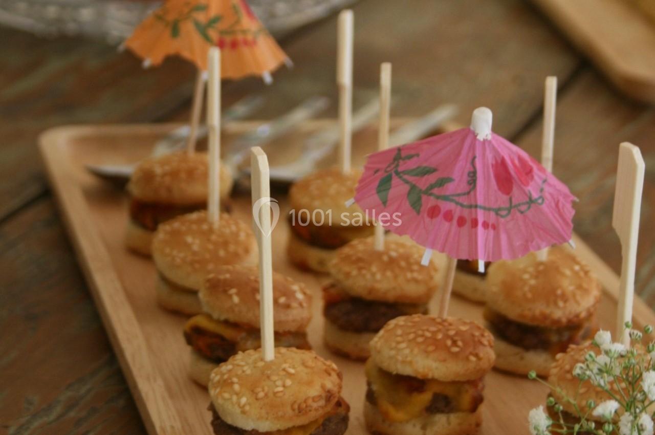 Mini-burgers sur un plateau en bois, garnis de piques et de petits parasols colorés, disposés sur une table en bois.