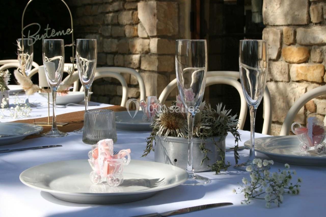 Table décorée pour un baptême avec nappes blanches, verres à pied, fleurs séchées et petits landaus en plastique rose.
