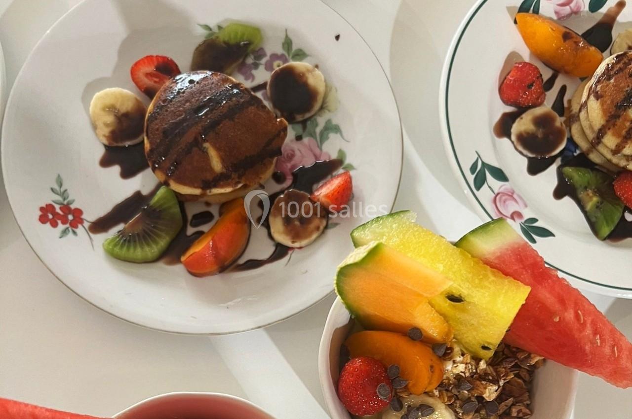 Assiette de pancakes garnis de fruits frais et sauce chocolat, accompagnée d'un bol de granola et fruits variés.