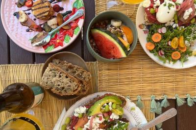 Salon lumineux avec canapé turquoise, coussins colorés, télévision, tapis en fibres naturelles et vue sur une cuisine…