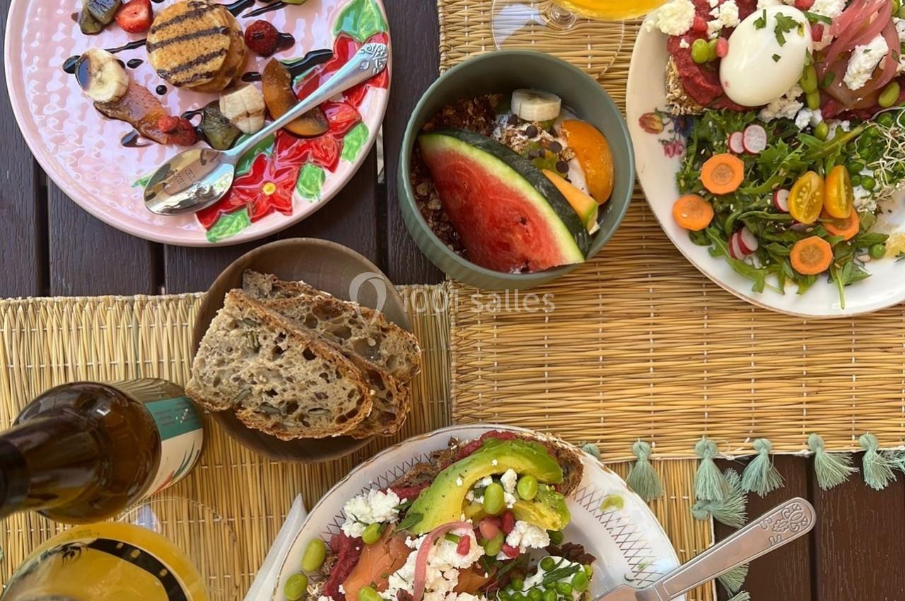 Repas coloré composé de salades, fruits, pain et boissons, disposé sur une table en bois avec sets en paille.