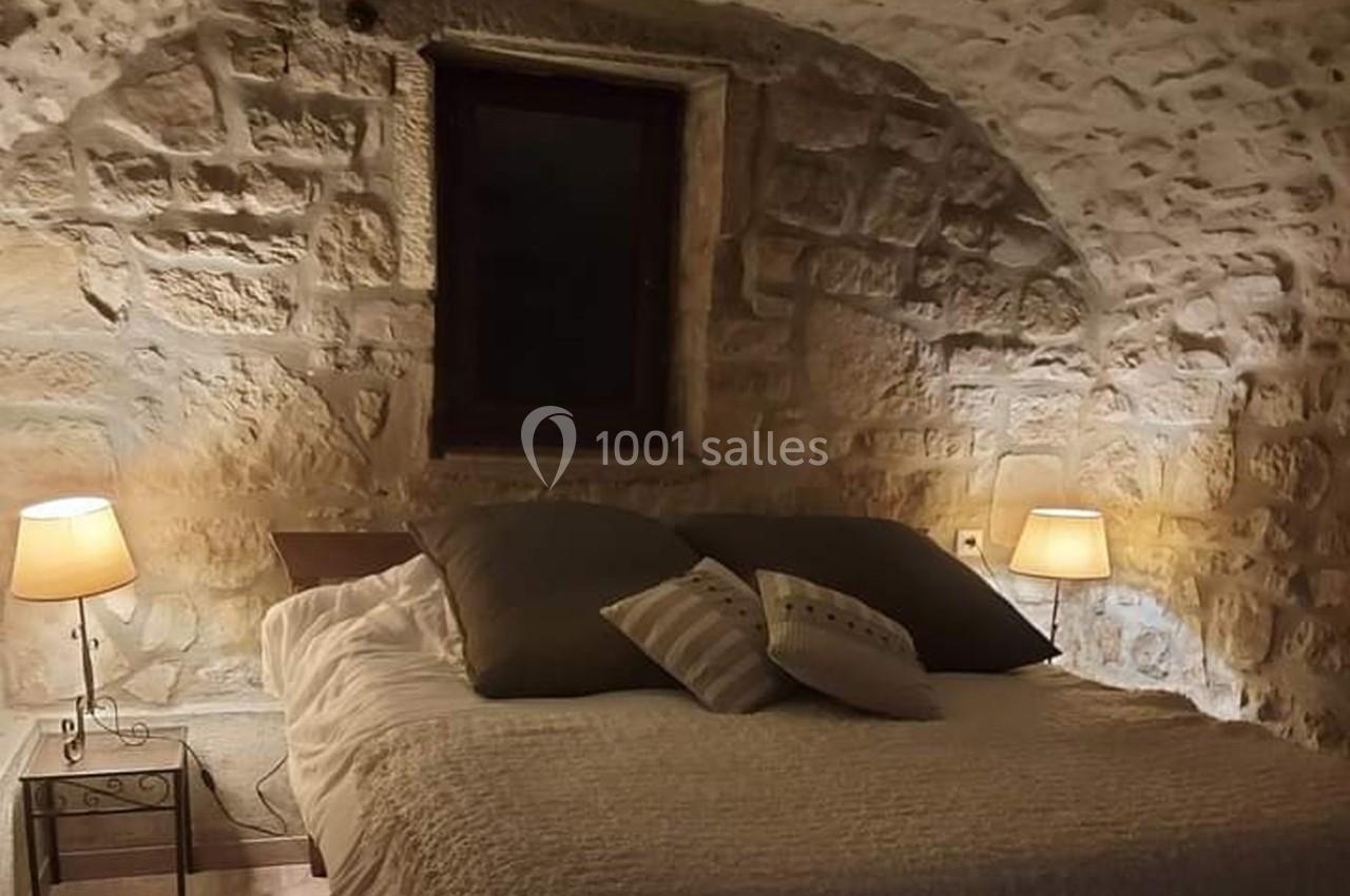 Chambre avec murs en pierre apparente, lit double, coussins et éclairage doux par deux lampes de chevet.
