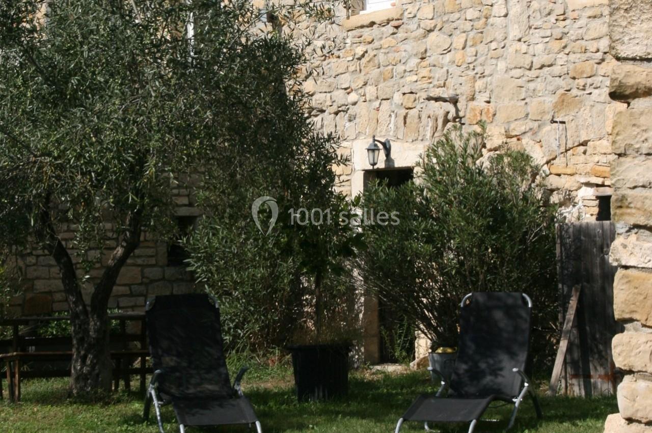 Deux chaises longues noires installées sur une pelouse, entourées d'arbres et d'un mur en pierre.