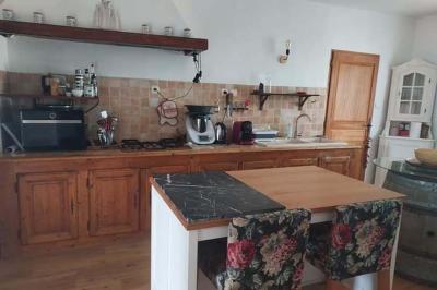 Salon lumineux avec canapé turquoise, coussins colorés, télévision, tapis en fibres naturelles et vue sur une cuisine…