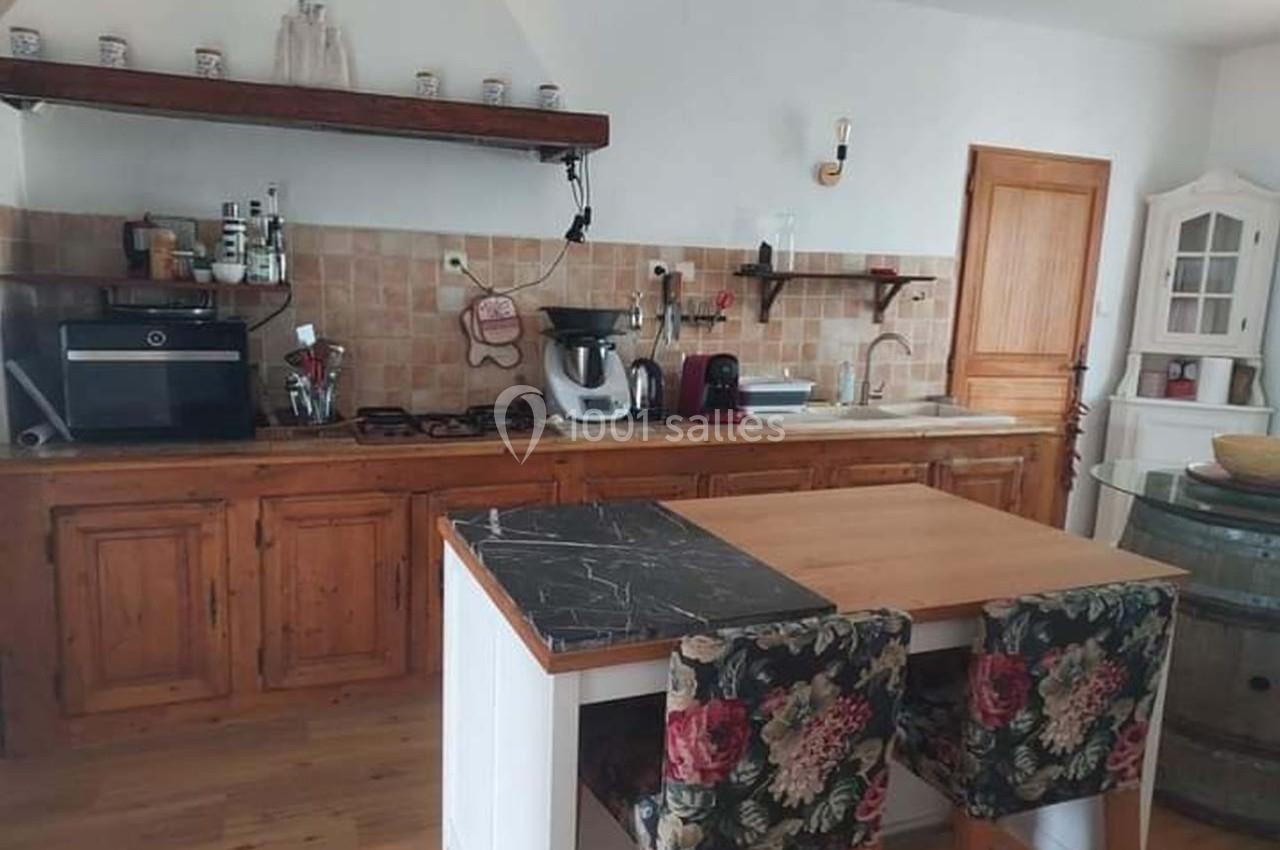 Cuisine rustique avec meubles en bois, plan de travail, électroménagers modernes et table avec chaises rembourrées.