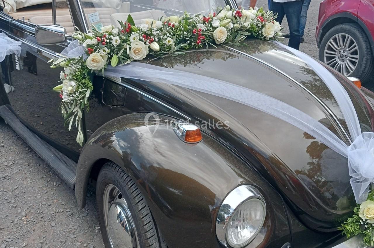 Voiture ancienne décapotable noire ornée de fleurs blanches et vertes, entourée de personnes en extérieur.
