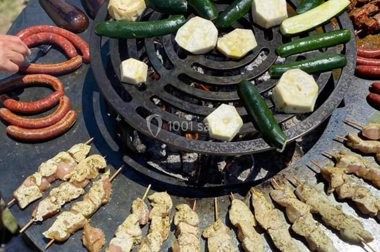 Viandes, légumes et saucisses grillés sur une plancha ronde avec des brochettes de poulet au premier plan.