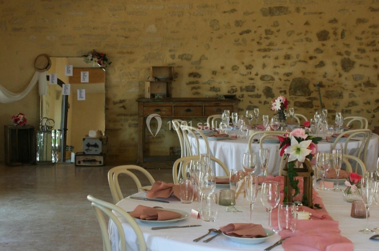 Salle de réception décorée avec des tables rondes, nappes blanches, serviettes roses et fleurs en centre de table.