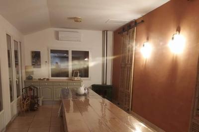 Salon lumineux avec canapé turquoise, coussins colorés, télévision, tapis en fibres naturelles et vue sur une cuisine…