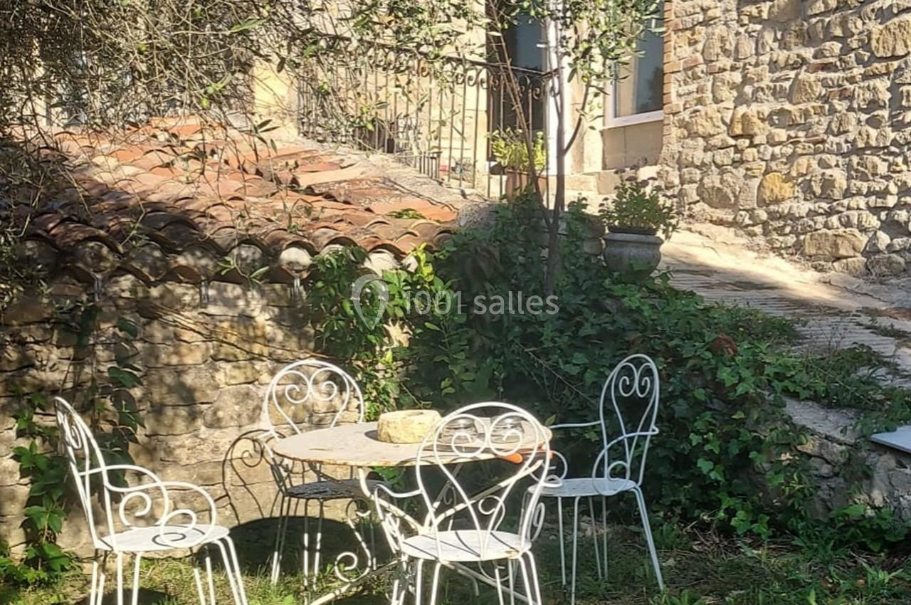 Mobilier de jardin en fer forgé blanc disposé autour d'une table ronde, près d'un mur en pierre et d'un escalier extérieur.
