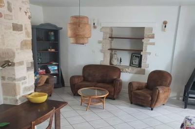 Salon lumineux avec canapé turquoise, coussins colorés, télévision, tapis en fibres naturelles et vue sur une cuisine…