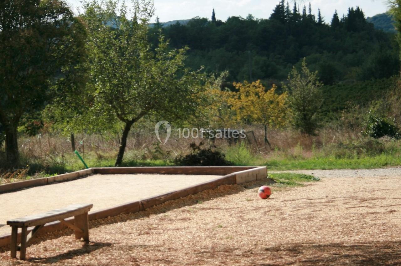 Terrain de pétanque en plein air entouré de végétation, avec un banc en bois et un ballon au sol.