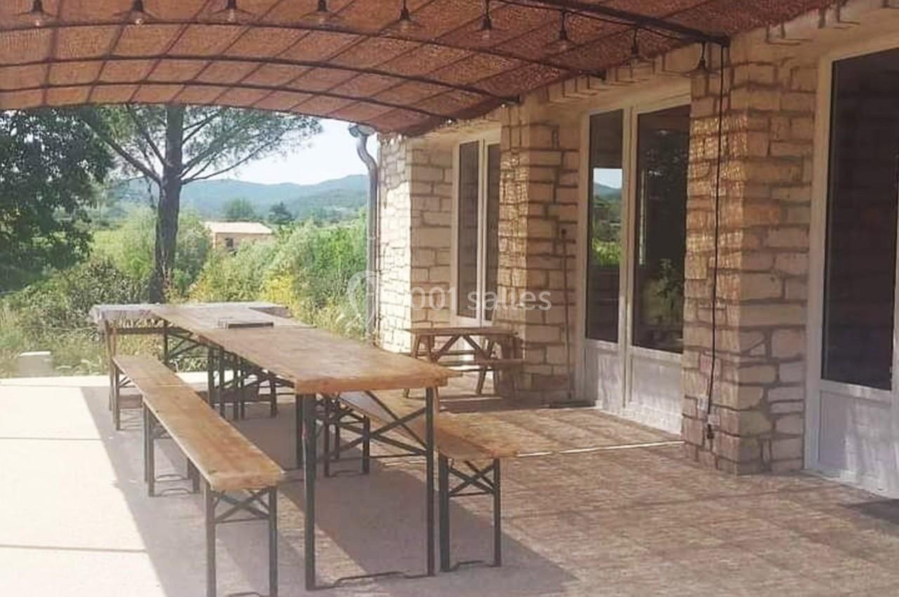 Terrasse ensoleillée avec tables et bancs en bois sous une pergola, entourée de verdure et d'un paysage rural.