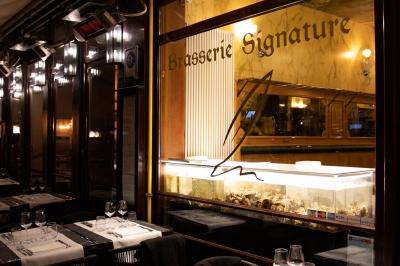 Salle de restaurant avec tables dressées, banquettes en bois, bar en bois et étagères garnies de verres et bouteilles.